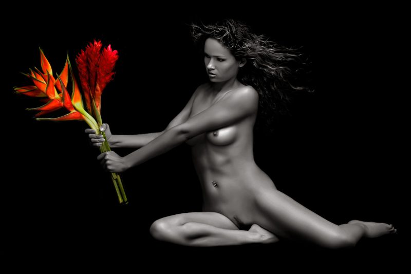 A nude woman holding orange and red flowers.