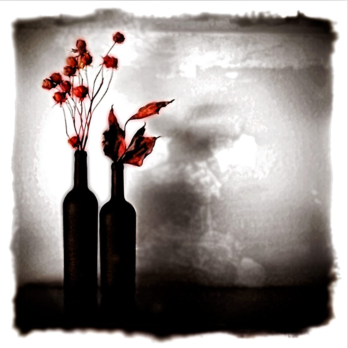 A black and white photo of two bottles with flowers.