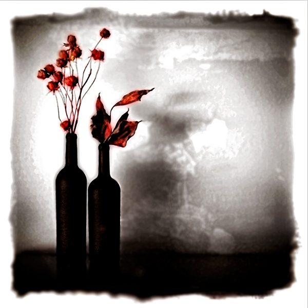 A black and white photo of two bottles with flowers.