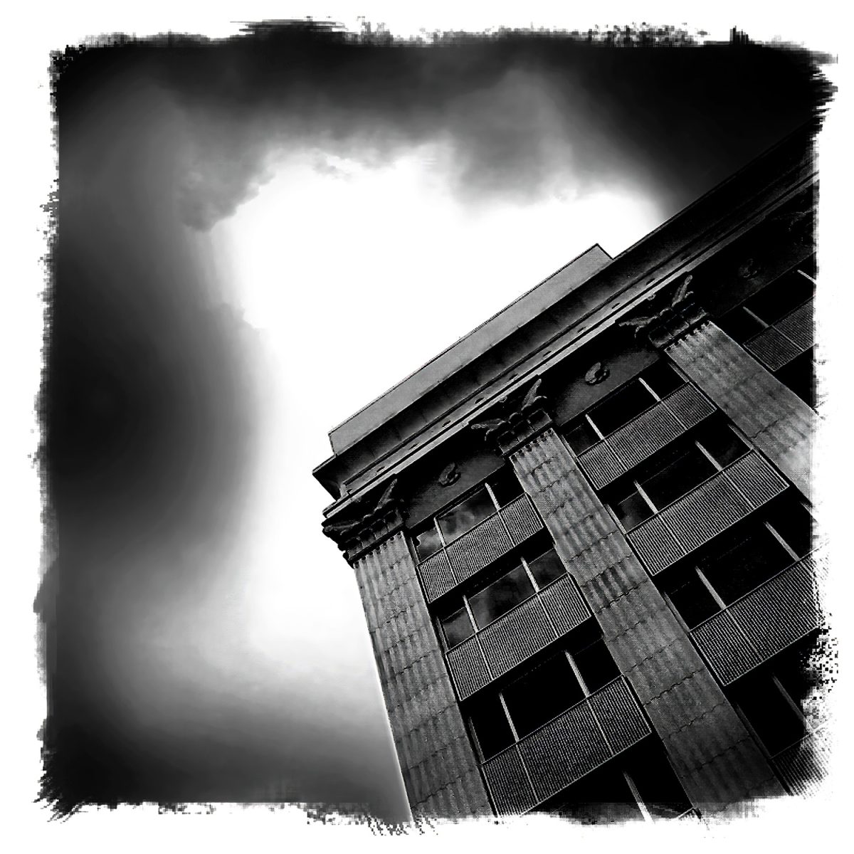 A black and white photo of a building with clouds in the sky.
