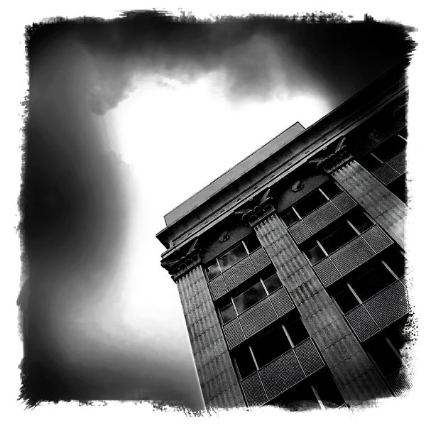 A black and white photo of a building with clouds in the sky.