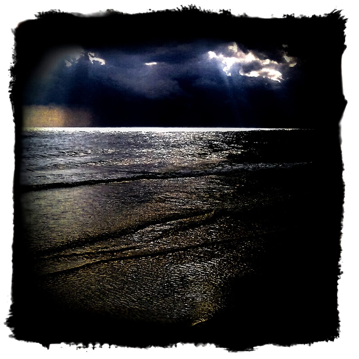 A dark stormy sky over the ocean with sunbeams shining through.