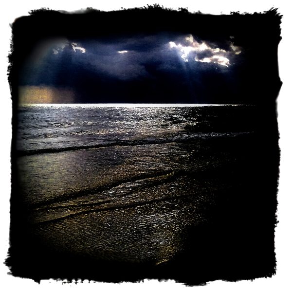 A dark stormy sky over the ocean with sunbeams shining through.
