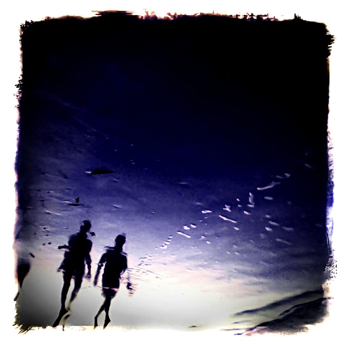 Two people walking on the beach in the late evening.