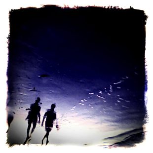Two people walking on the beach in the late evening.
