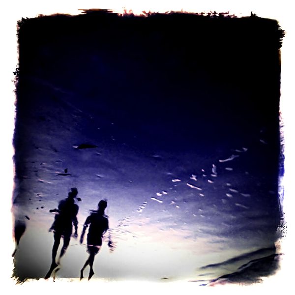 Two people walking on the beach in the late evening.