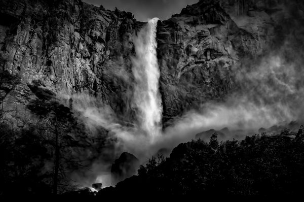 Raging black and white waterfall cascading down rugged mountain cliffs, dramatic nature landscape.