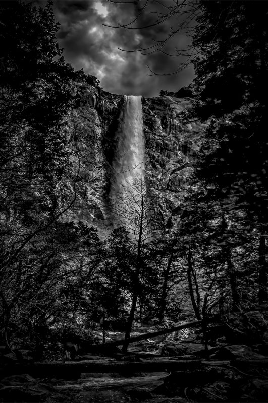Misty waterfall surrounded by trees in a black and white landscape.