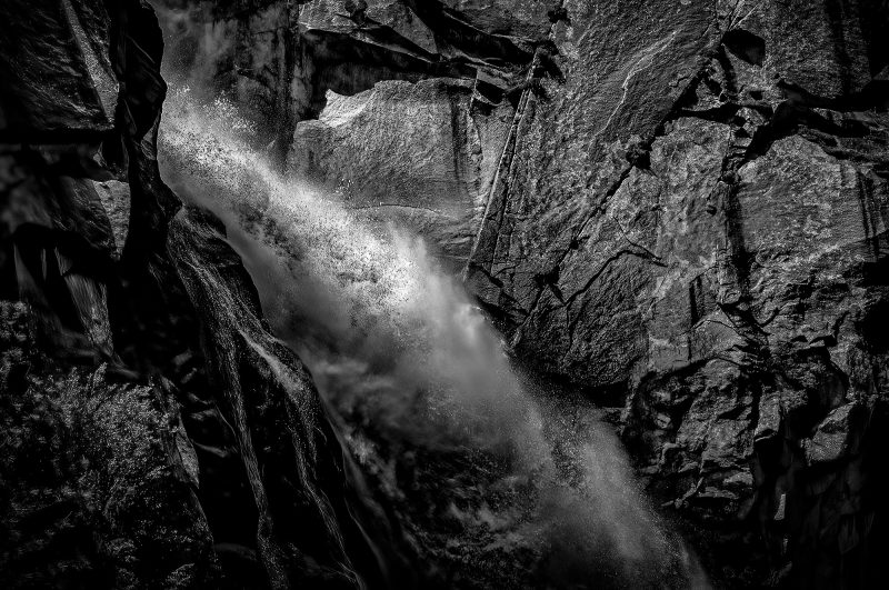 Rugged mountain waterfall in black and white, showcasing dramatic natural rock formations and cascading water.