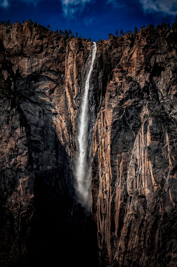 Flowing waterfall cascading down rugged cliffside in Yosemite National Park.