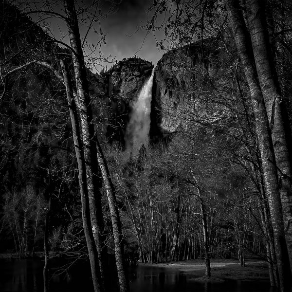 Dark waterfall cascading in a rugged mountain landscape, black and white fine art photograph.