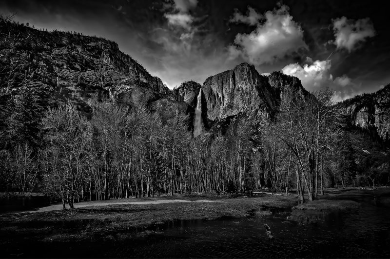 Vivid black and white landscape of Upper Yosemite Falls with dramatic clouds and tall trees, part of The Doug Heslep Fine Art Collection.