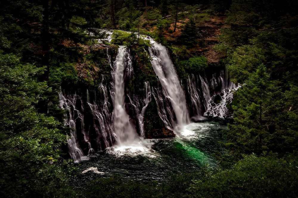 Majestic waterfall surrounded by lush green forest in the Doug Heslep Fine Art Collection.