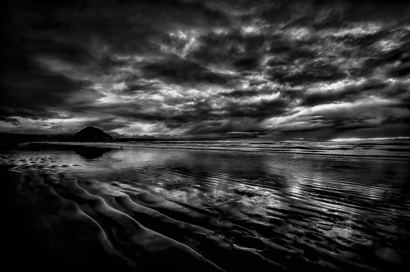 Dark moody beach landscape with dramatic stormy sky, black and white ocean waves, and rugged shoreline, part of The Doug Heslep Fine Art Collection.