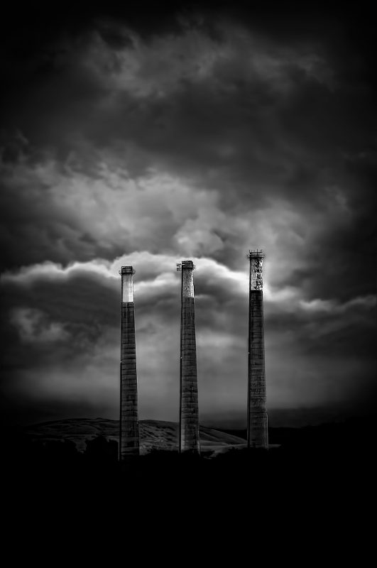 Industrial landscape art featuring three smokestacks with dramatic, moody skies.
