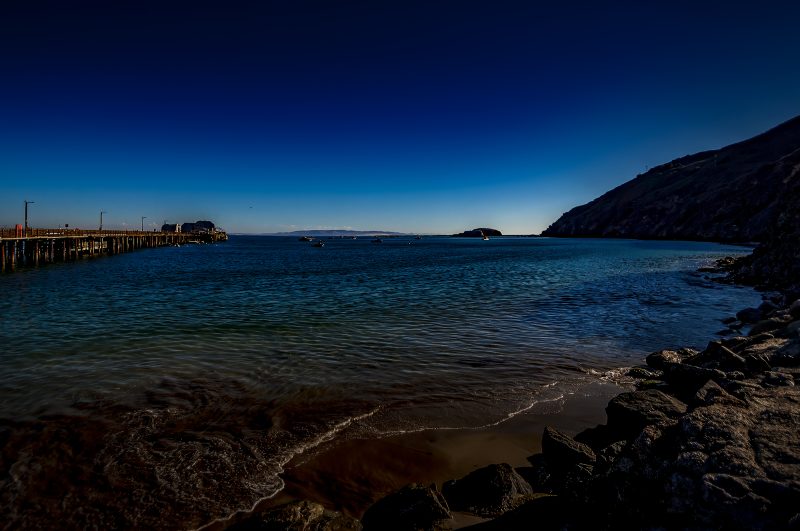 Calm ocean shoreline with pier and boats at sunset, beautiful coastal scenery.