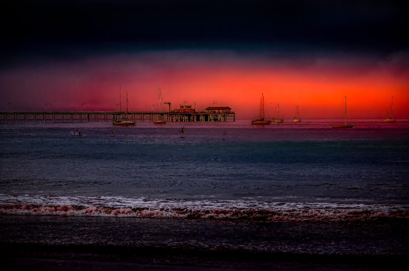 Colorful sunset over a pier with sailboats, vibrant ocean scene, featuring realistic maritime artwork.