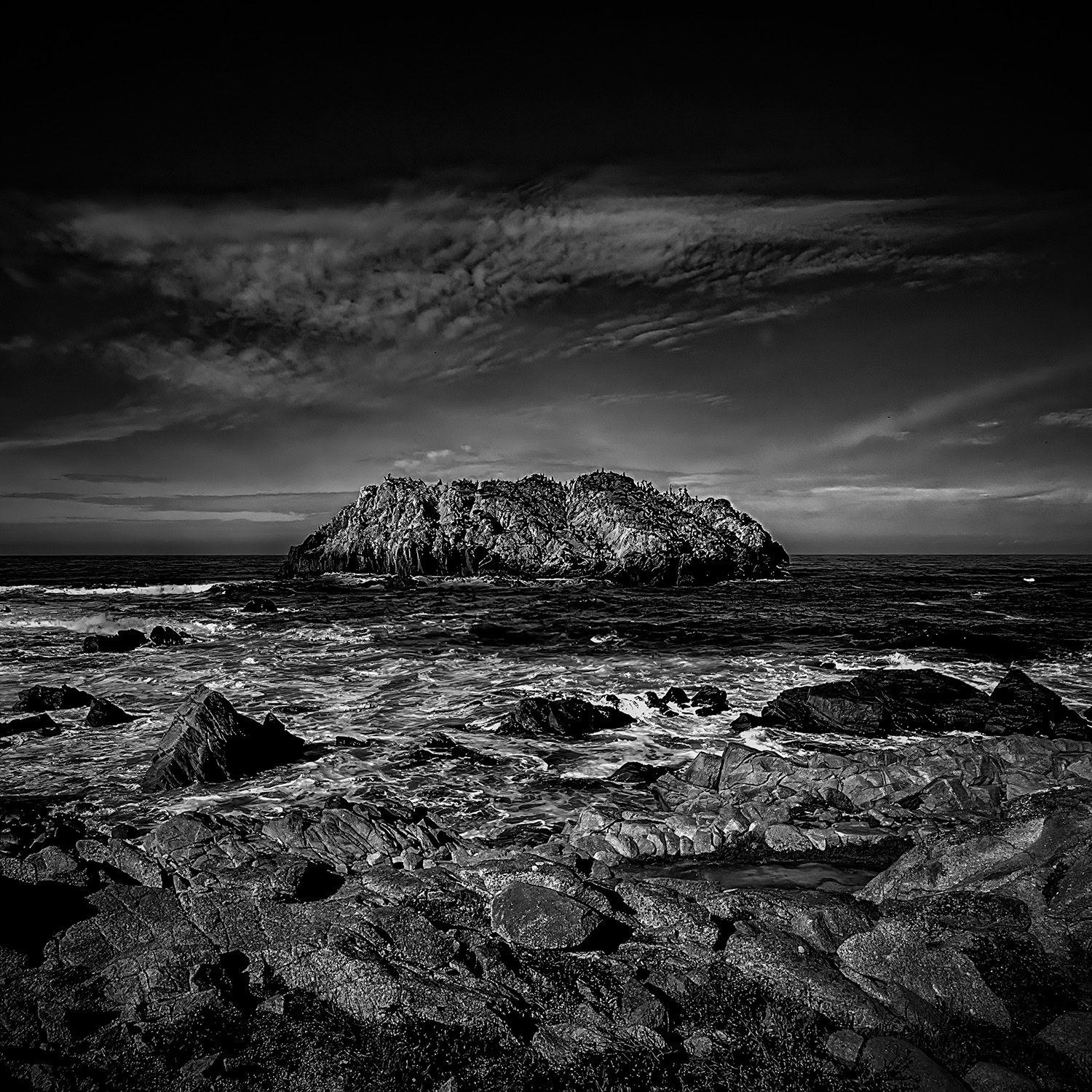 Rugged coastal rocks with island landscape in black and white, part of The Doug Heslep Fine Art Collection.
