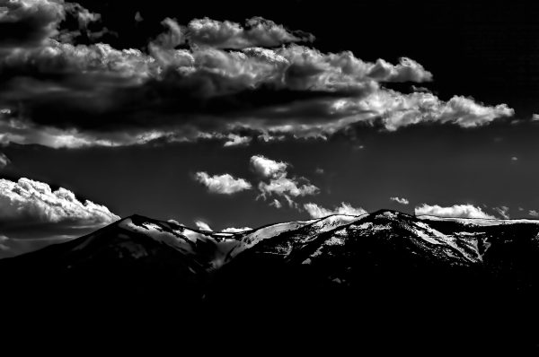 Snow-capped mountain landscape with dramatic cloud cover, black and white nature photography, stunning wilderness scene.