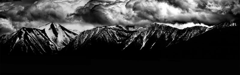 Snow-capped mountain range under stormy dark clouds, black and white landscape artwork