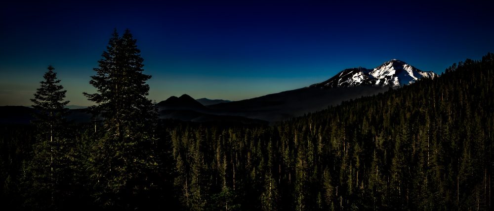 Majestic mountain landscape with snow-capped peaks and dense evergreen forest.