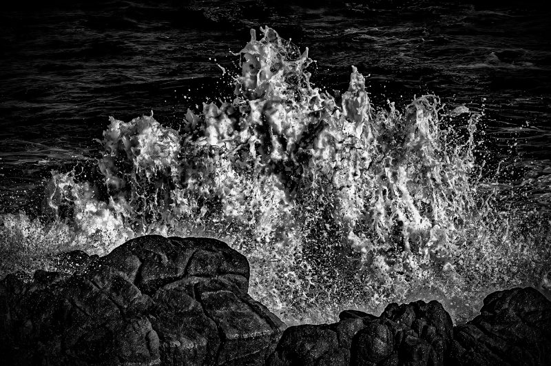 Vibrant black and white photo of ocean waves crashing against rocks, capturing natural beauty and movement.