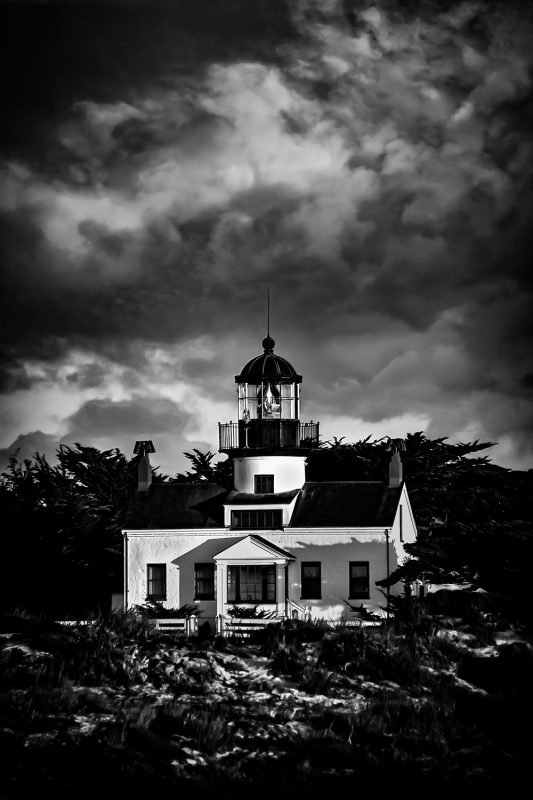Lighthouse at night in black and white with dramatic cloud sky.