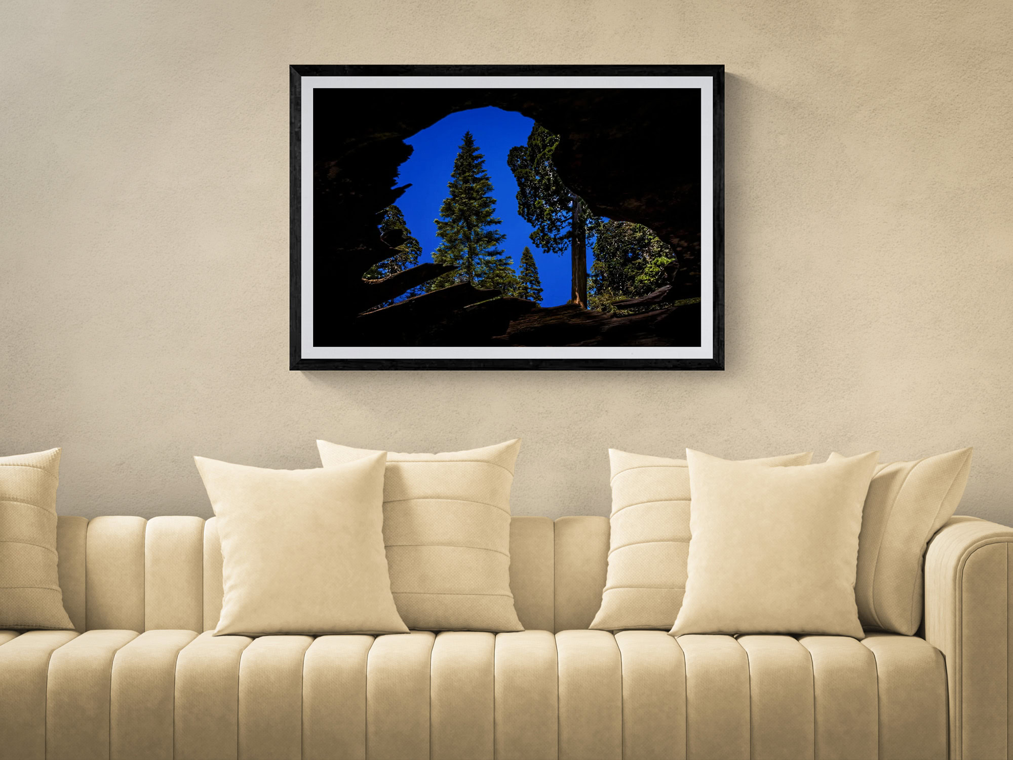 Silhouette of trees and mountain landscape in a black frame, hanging above a beige sofa.