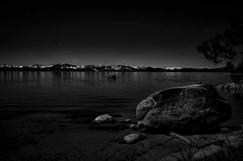 Serene mountain lake with snow-capped peaks, black and white landscape photography, tranquil water, natural beauty.