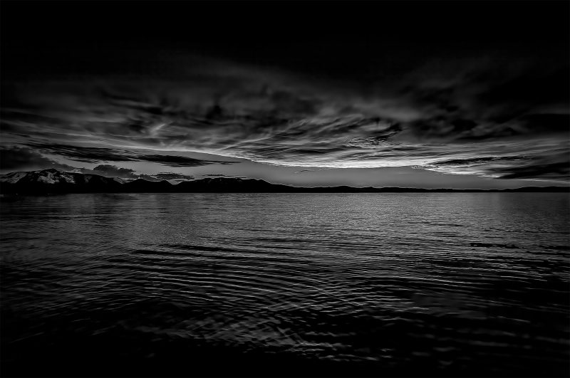 Dark landscape photograph by Doug Heslep, evocative black and white seascape with mountains and dramatic sky.