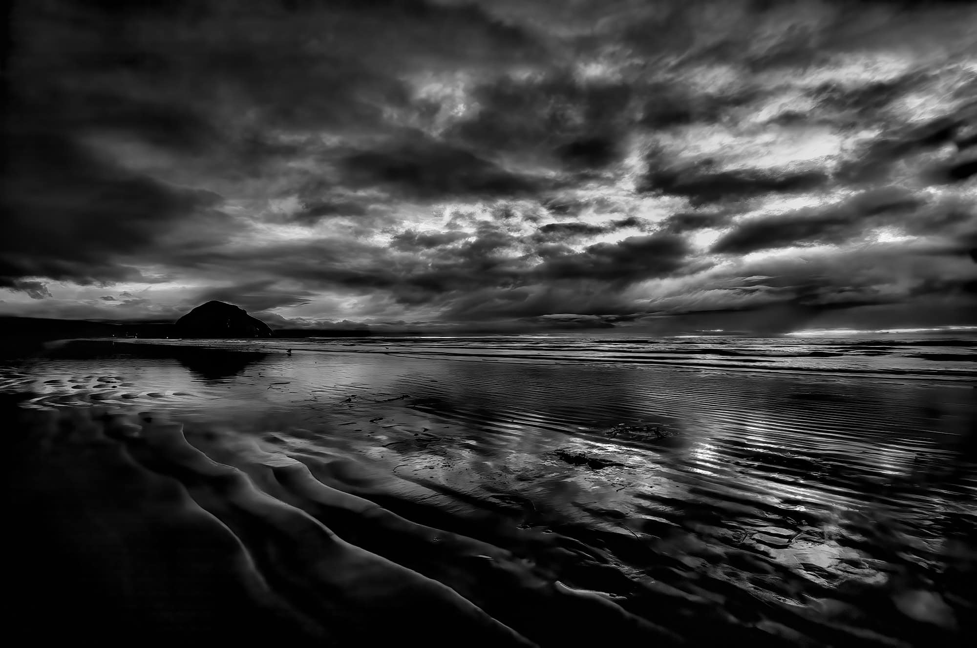 Black and White photo of Morro Rock silhouetted by a soothing sunset as seen from Morro Strand State Beach