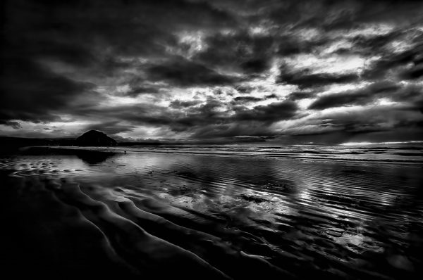 Black and White photo of Morro Rock silhouetted by a soothing sunset as seen from Morro Strand State Beach