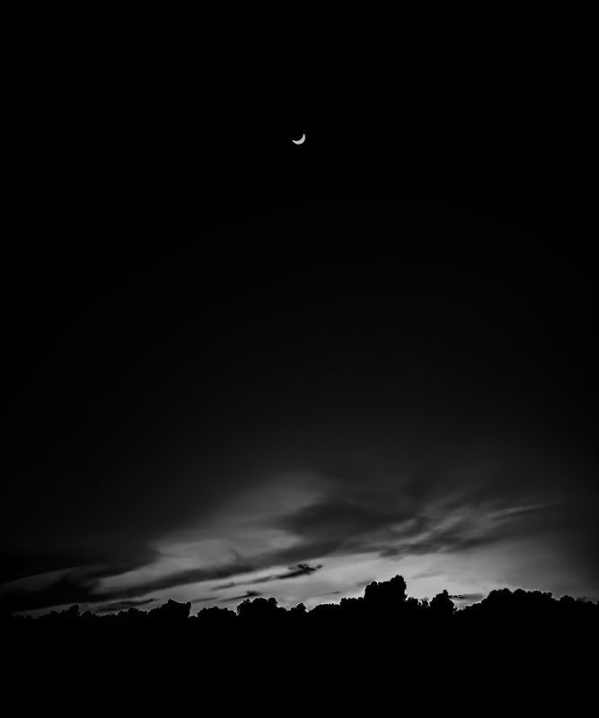 Moon crescent over a dark night sky, atmospheric landscape image from The Doug Heslep Fine Art Collection.