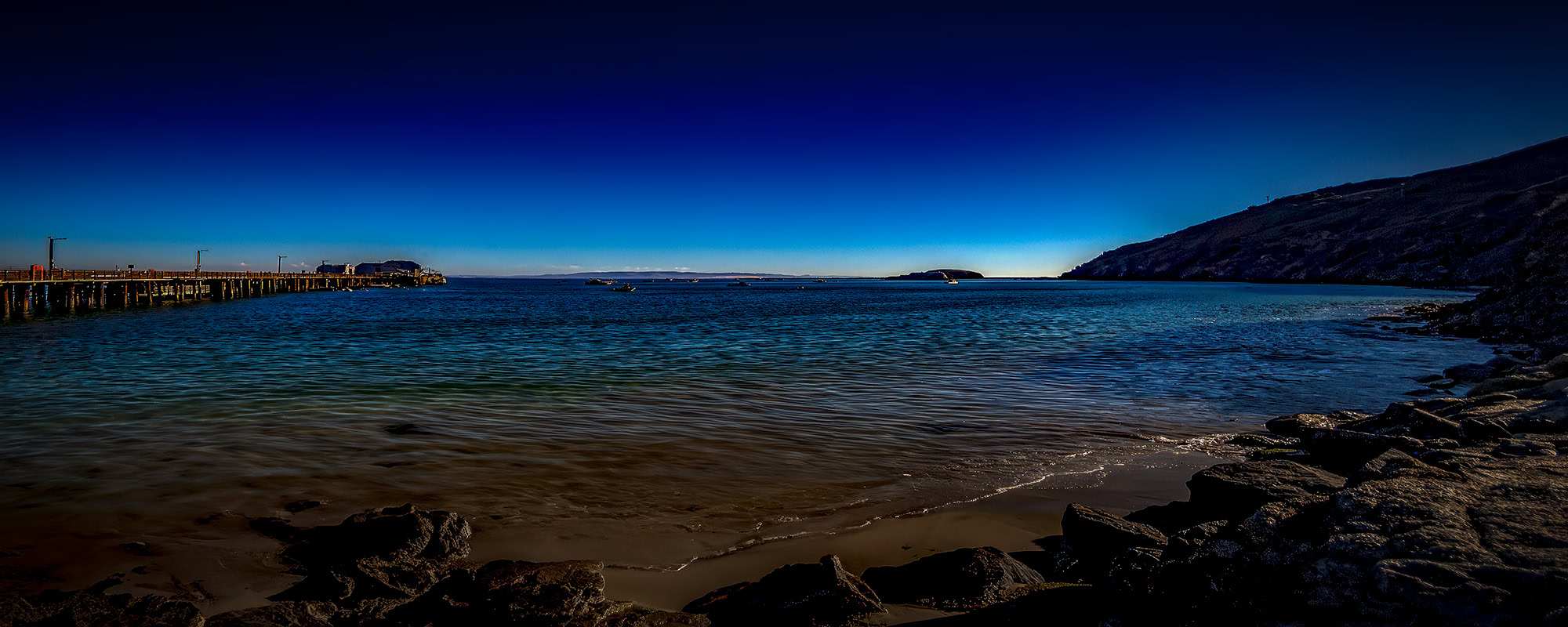 Calm ocean shoreline with pier and boats at sunset, beautiful coastal scenery.