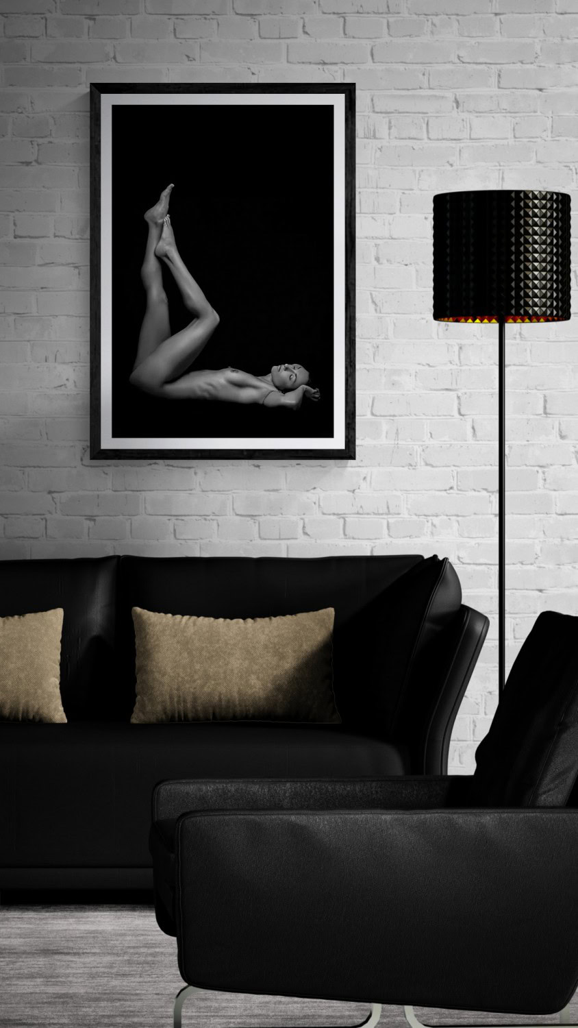 Elegant black-and-white nude photograph of a woman with legs crossed, displayed in a modern interior.